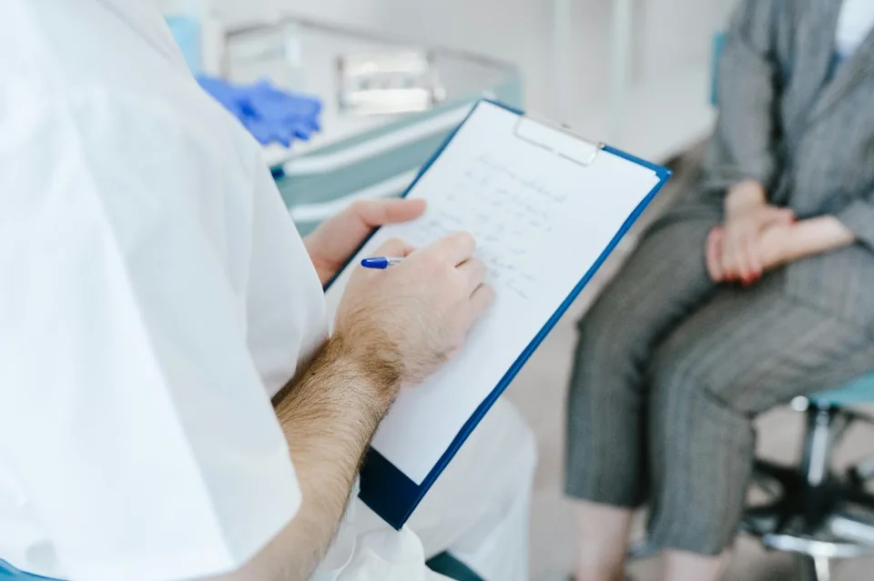 Clinician writing on a clipboard during a patient consultation